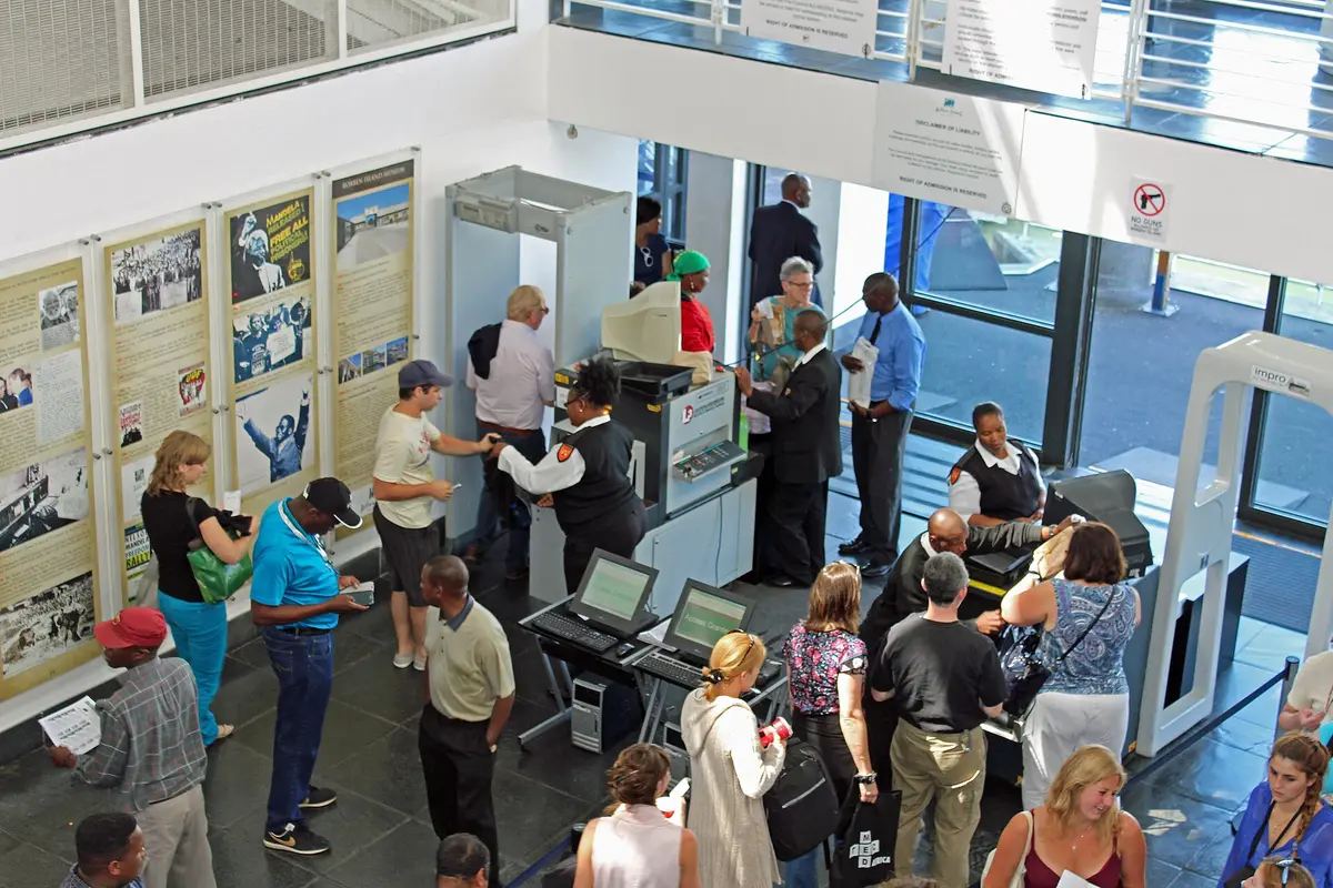 Visitors queuing for security and ticket checks inside the Nelson Mandela Gateway, beside display panels of historic photographs