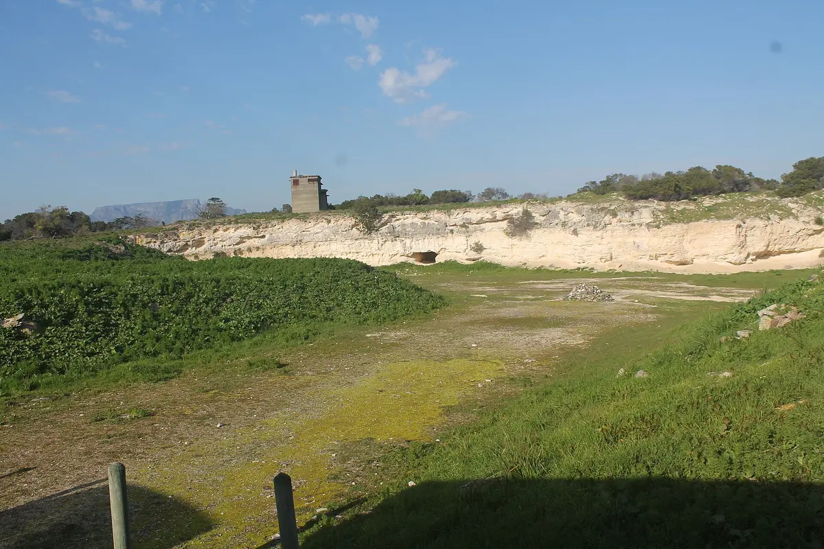 The pale cliff of the old lime quarry on Robben Island above a grassy floor, with a small stone hut on the rim and a blue sky