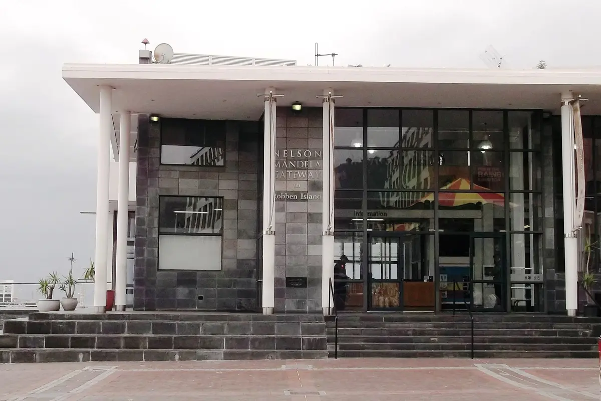 The front of the Nelson Mandela Gateway to Robben Island, a low modern building with white columns, dark stone walls and a sign on the facade